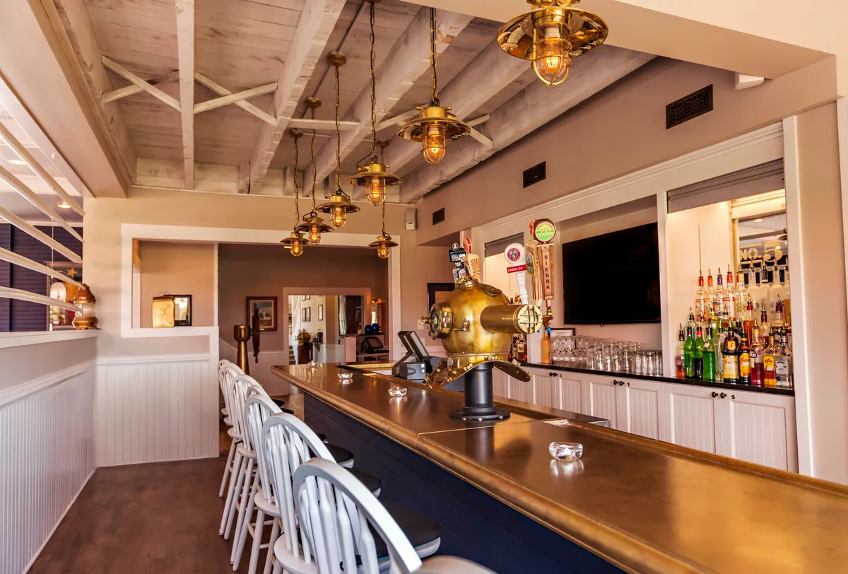 Showcasing a brass bar counter under glowing pendant lights, with a vibrant display of bottled liquors, this interior scene is energetic and inviting. Guests can be seen enjoying drinks and light bites, creating an atmosphere ideal for sunset cocktails or after-adventure relaxation.